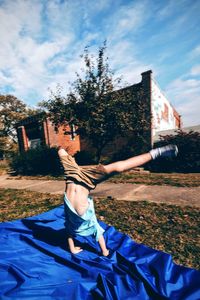 Full length of boy performing handstand on blue fabric in yard
