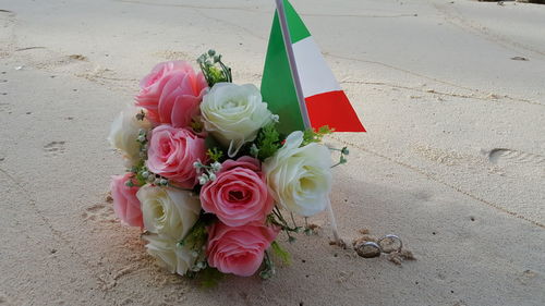 Wedding rings with rose bouquet and italian flag on sandy beach
