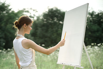 Side view of woman holding book while standing against sky