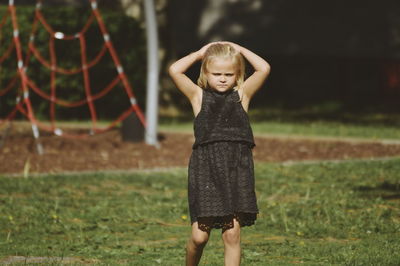 Portrait of cute girl with hands behind head standing on grassy field