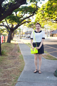Full length of cheerful young woman standing on footpath