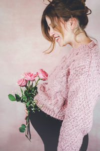 Midsection of woman holding pink rose at home