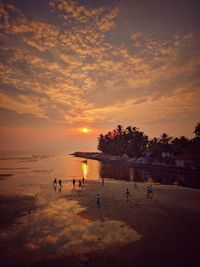 People at beach against sky during sunset