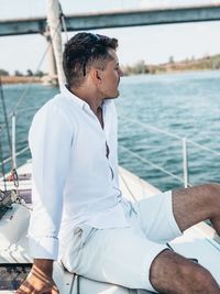 Man sitting on yacht in sea against bridge