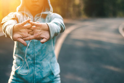 Woman stretching hands while exercising on road