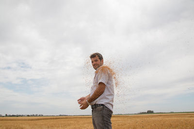 Portrait of smiling farmer throwing crops while standing on field