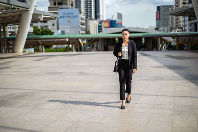 Full length portrait of businesswoman on footpath in city