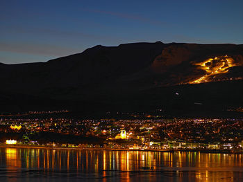 Illuminated city by river against sky at night