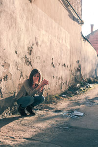 Young woman using mobile phone while sitting on wall