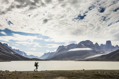 Silhouetted backpacker hikes along the shore of a mountain lake.