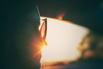 Close-up of young woman wearing eyeglasses sitting in car during sunset