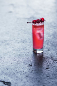 Tall pink cocktail drink with three raspberries on cocktail pick, concrete background
