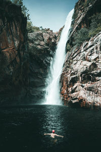 Man swimming in pond against of waterfall