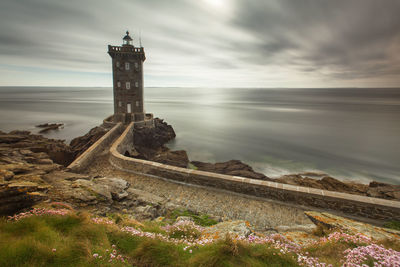 Lighthouse on pier by sea against sky