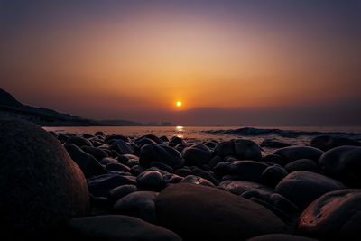 Rocks at sea shore against sky during sunset