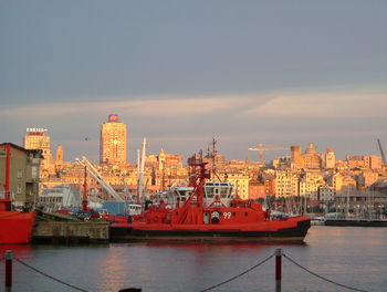 Boats in river by buildings against sky in city