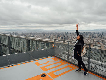 Woman with hand raised standing on building terrace against cityscape