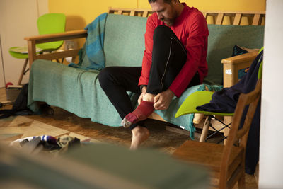 Man pulling up sock sitting on sofa at home