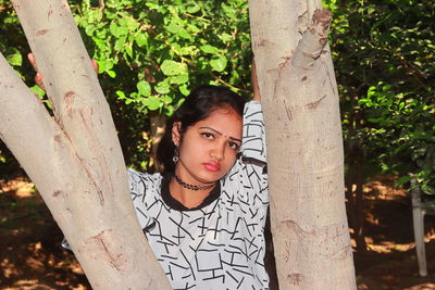 Portrait of woman standing by tree trunk