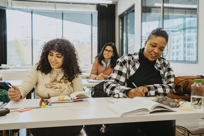 Female students writing while sitting at desks in classroom