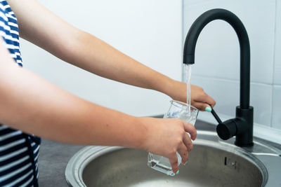 Midsection of woman filling drinking glass at sink