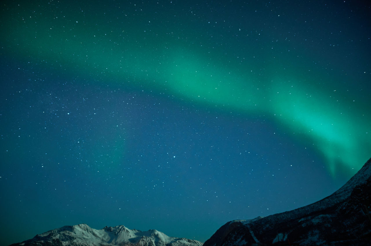 Low angle view of mountain and aurora borealis against sky at night