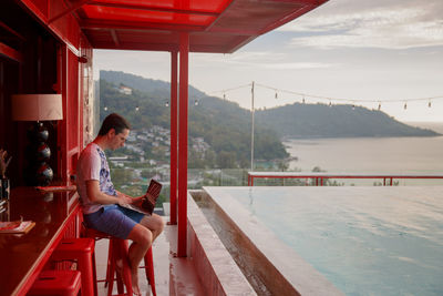 Side view of woman sitting on chair by sea