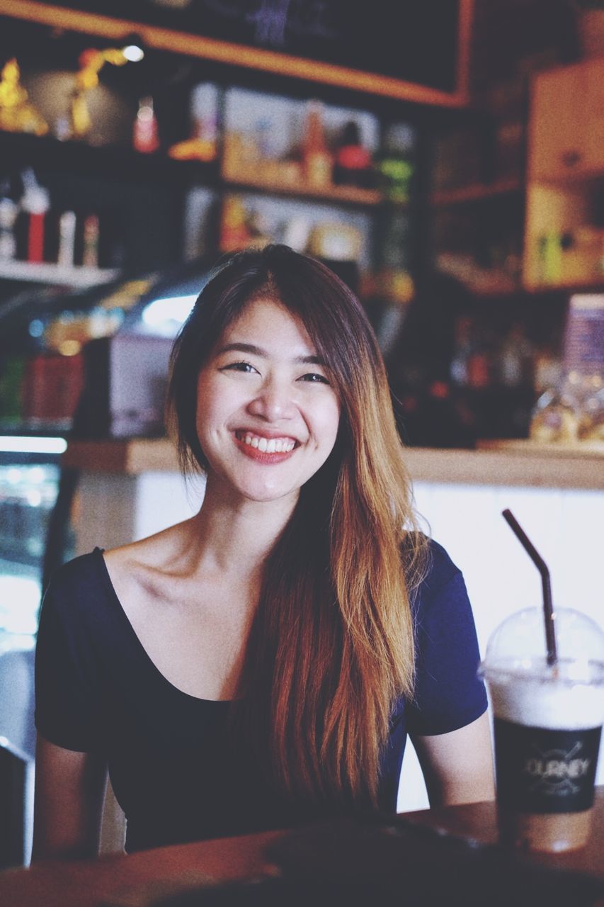 smiling, happiness, drink, sitting, indoors, restaurant, portrait, one person, table, long hair, looking at camera, real people, cheerful, food and drink, young adult, cafe, young women, beautiful woman, close-up, day, people