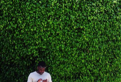 Man using mobile phone against ivy plants