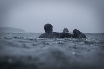 Rear view of man surfing in sea against sky during rainy season