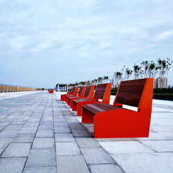 Empty chairs on footpath against sky