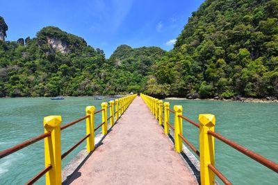 Diminishing perspective of footbridge over sea against mountains during sunset