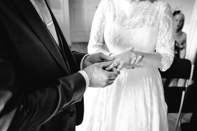 Midsection of bridegroom putting ring on bride during wedding ceremony