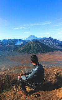 Rear view of woman sitting on mountain against sky