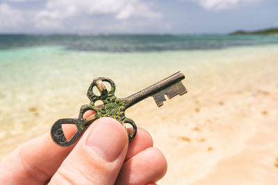 Cropped hand of person holding key at beach against sky