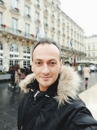 Portrait of smiling man in fur coat standing against building in city