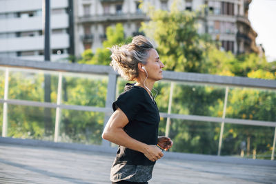 Side view of woman jogging while listening music at bridge