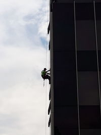 Low angle view of people working on building against sky