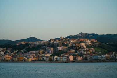 Houses on mountain by sea against clear sky during sunset