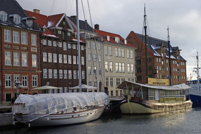 Sailboats moored on river by buildings against sky