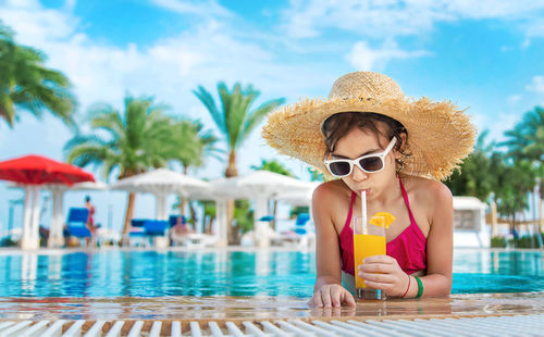 Girl wearing straw hat drinking orange juice at poolside