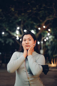 Portrait of young woman standing against illuminated christmas tree