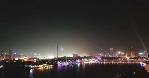 Illuminated buildings by river against sky at night