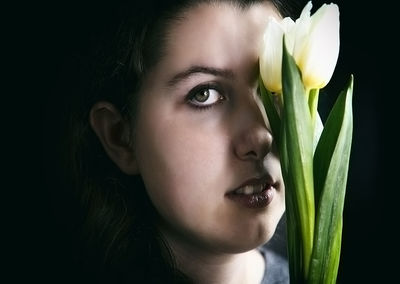Close-up portrait of woman with flower against black background