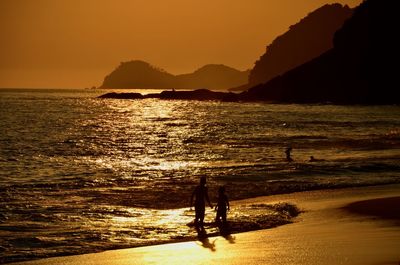 Silhouette people on beach against sky during sunset