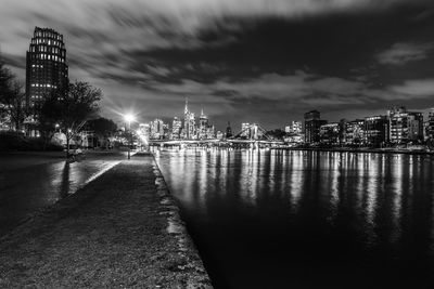 Illuminated buildings by river against sky in city