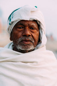 Varanasi, india - february, 2018: close-up portrait of elderly indian man wearing traditional white clothes standing on river bank