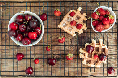 Fresh cherries in a bowl and strawberries with viennese waffles on a wooden table top view