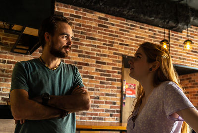 Smiling young couple standing in cozy bar and talking each other