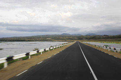 Road passing through landscape against cloudy sky